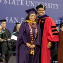 A woman and man in Commencement regalia smile at the camera