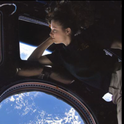 female astronaut in space looking out window at Earth