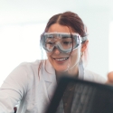 Person wearing goggles is smiling in a scientific lab.