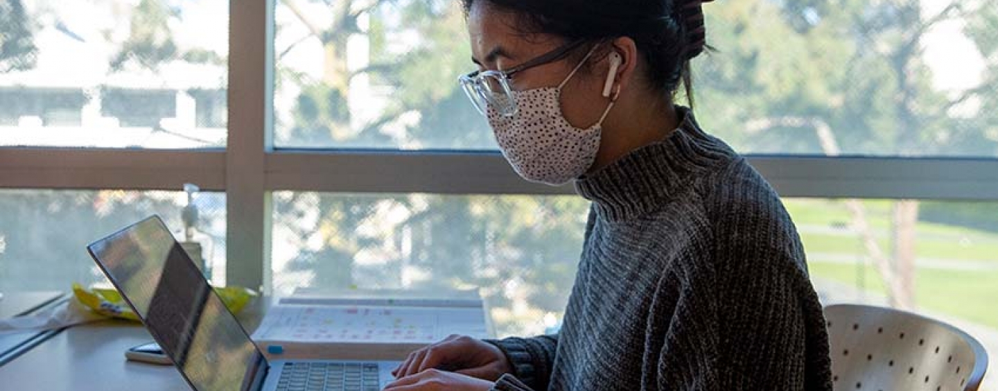 student wearing mask working on computer