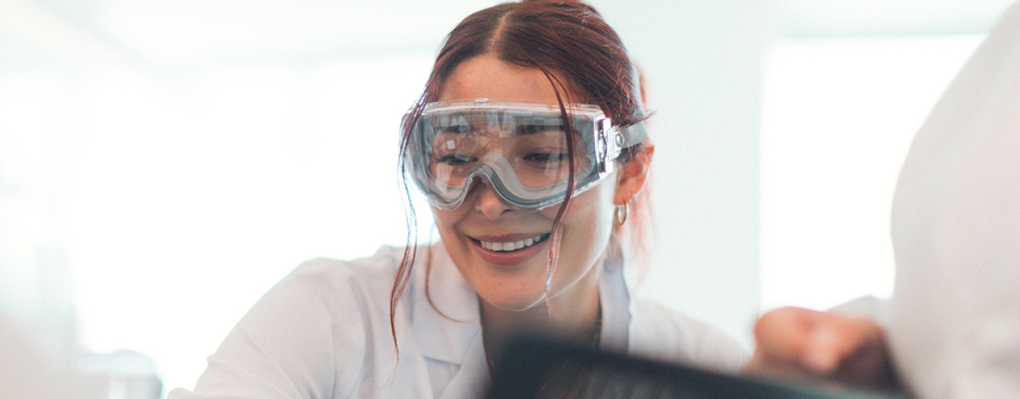 Person wearing goggles is smiling in a scientific lab.