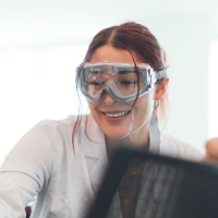 Person wearing goggles is smiling in a scientific lab.