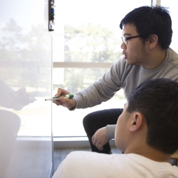 two students doing math on a white board