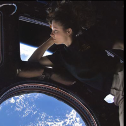 female astronaut in space looking out window at Earth